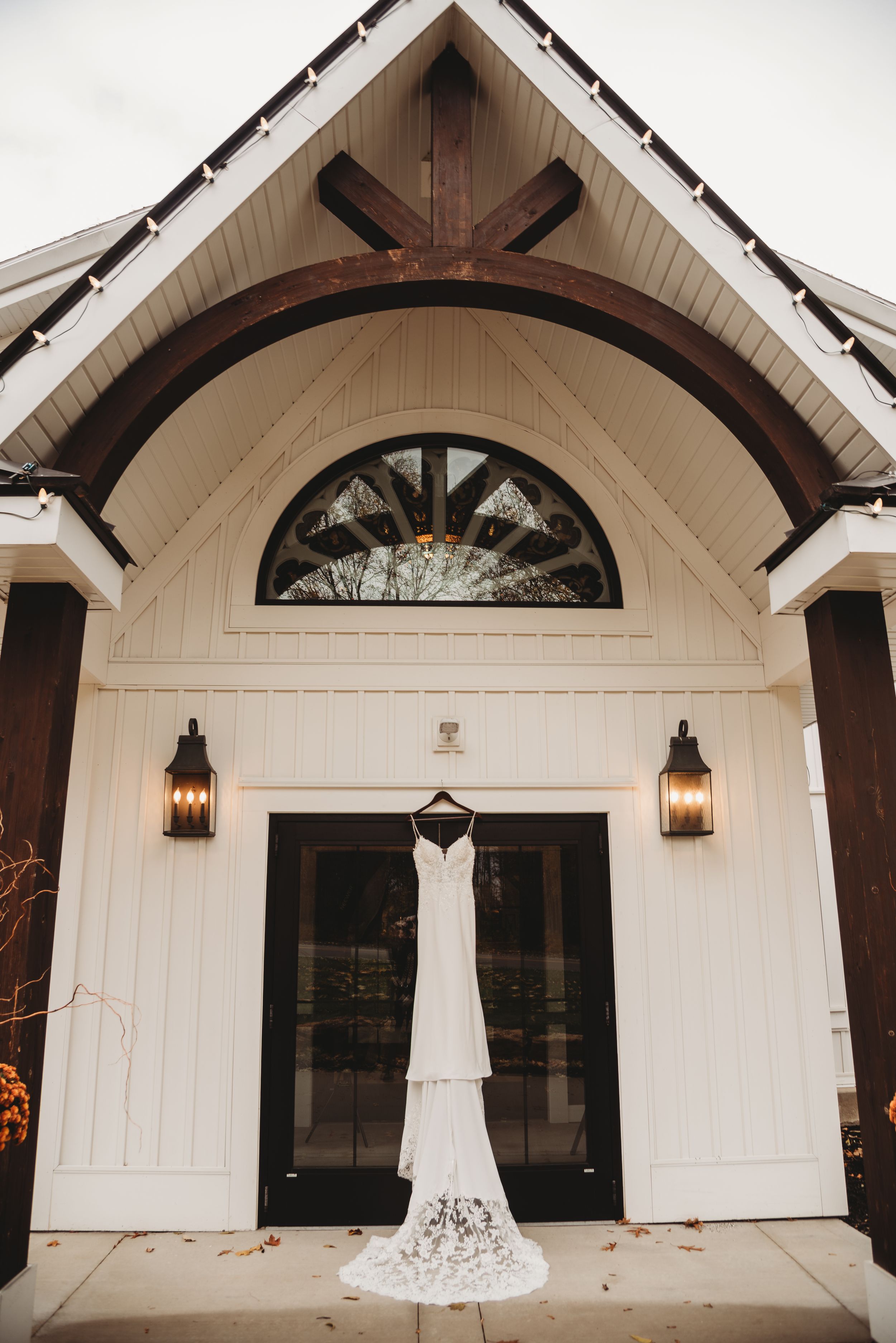 Elegant white wedding dress hanging on a hanger outside a charming white chapel entrance.