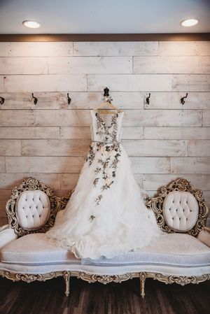 Elegant ball gown wedding dress with floral appliques hanging between ornate vintage chairs.