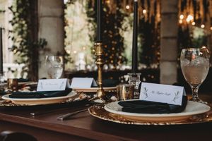 Elegant black and gold wedding reception table setting with candlesticks and place cards.