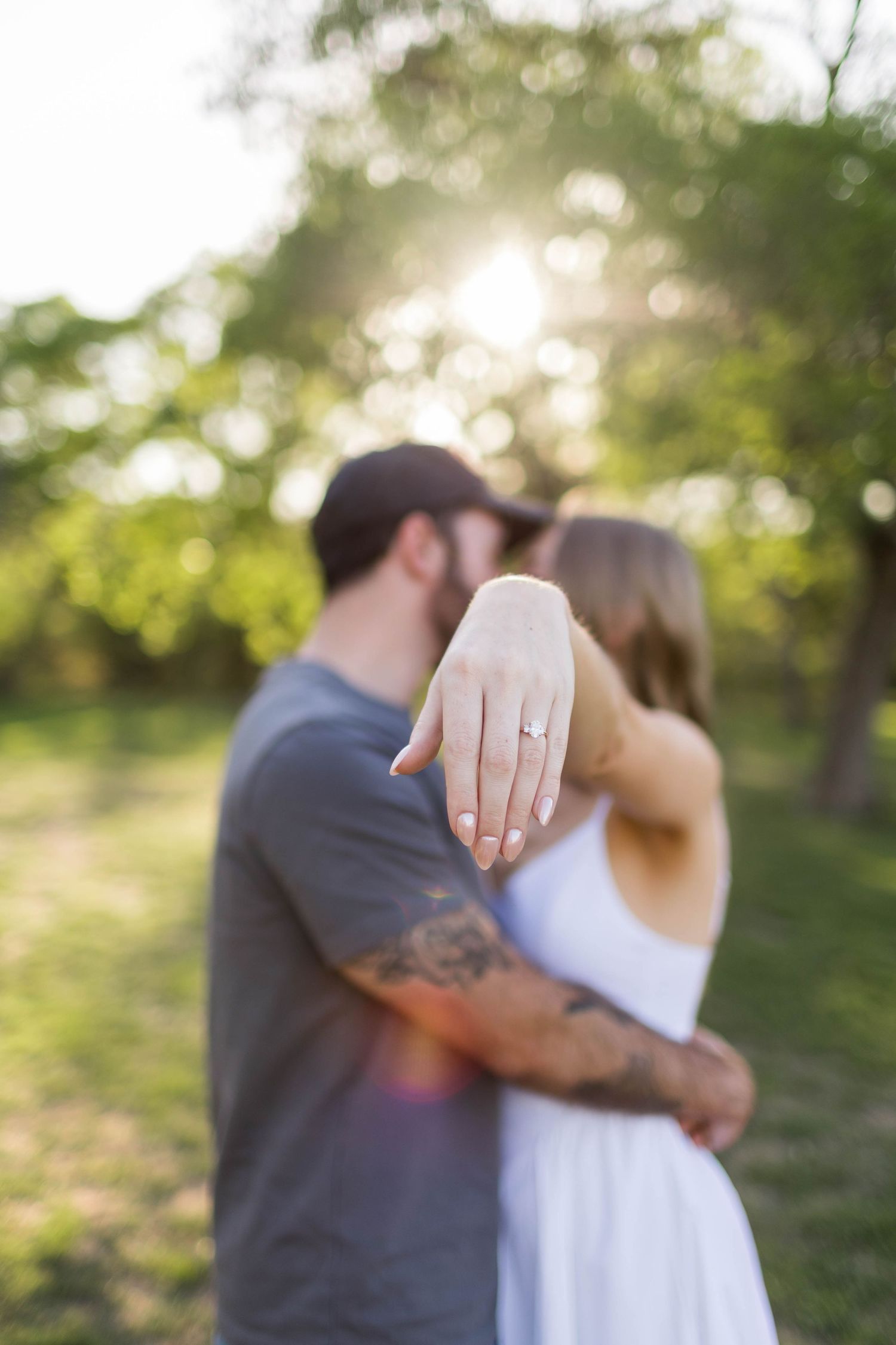 Couple embracing outdoors at sunset, woman displaying engagement ring on hand at Commons Ford Ranch taken by engagement photographer Nicole.