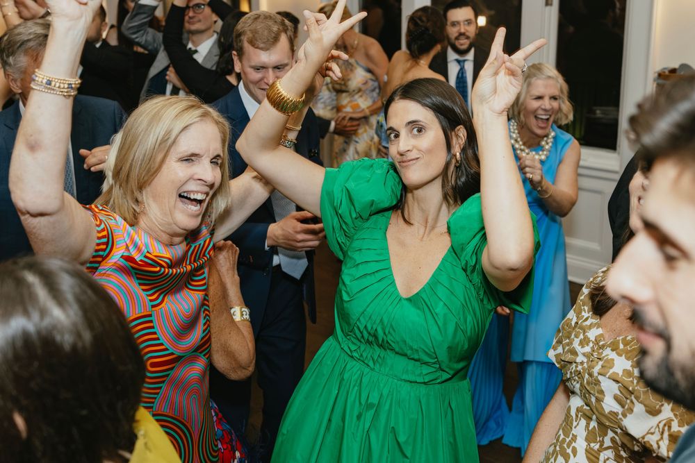 Guests dancing joyfully at a wedding reception, women in green and colorful dresses raising hands.