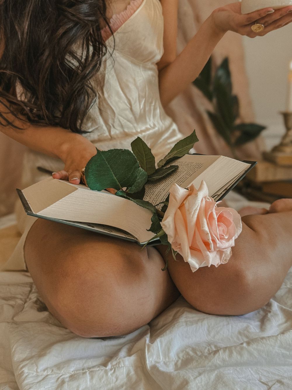 Woman sitting cross-legged holding open book with a peach rose placed between the pages.