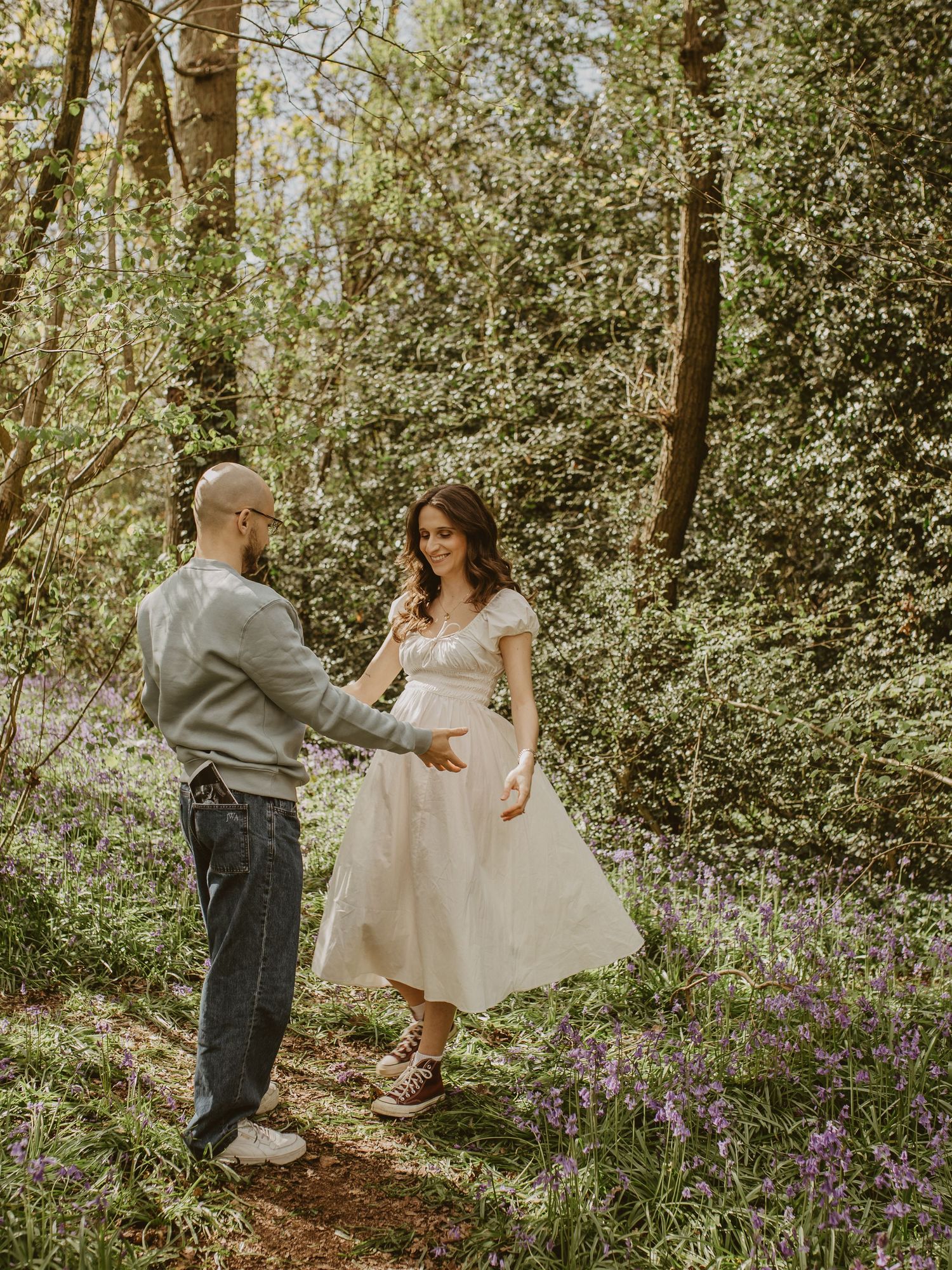 Couple sharing a tender moment in a bluebell woodland, man in grey sweatshirt touching woman's brown jumper.