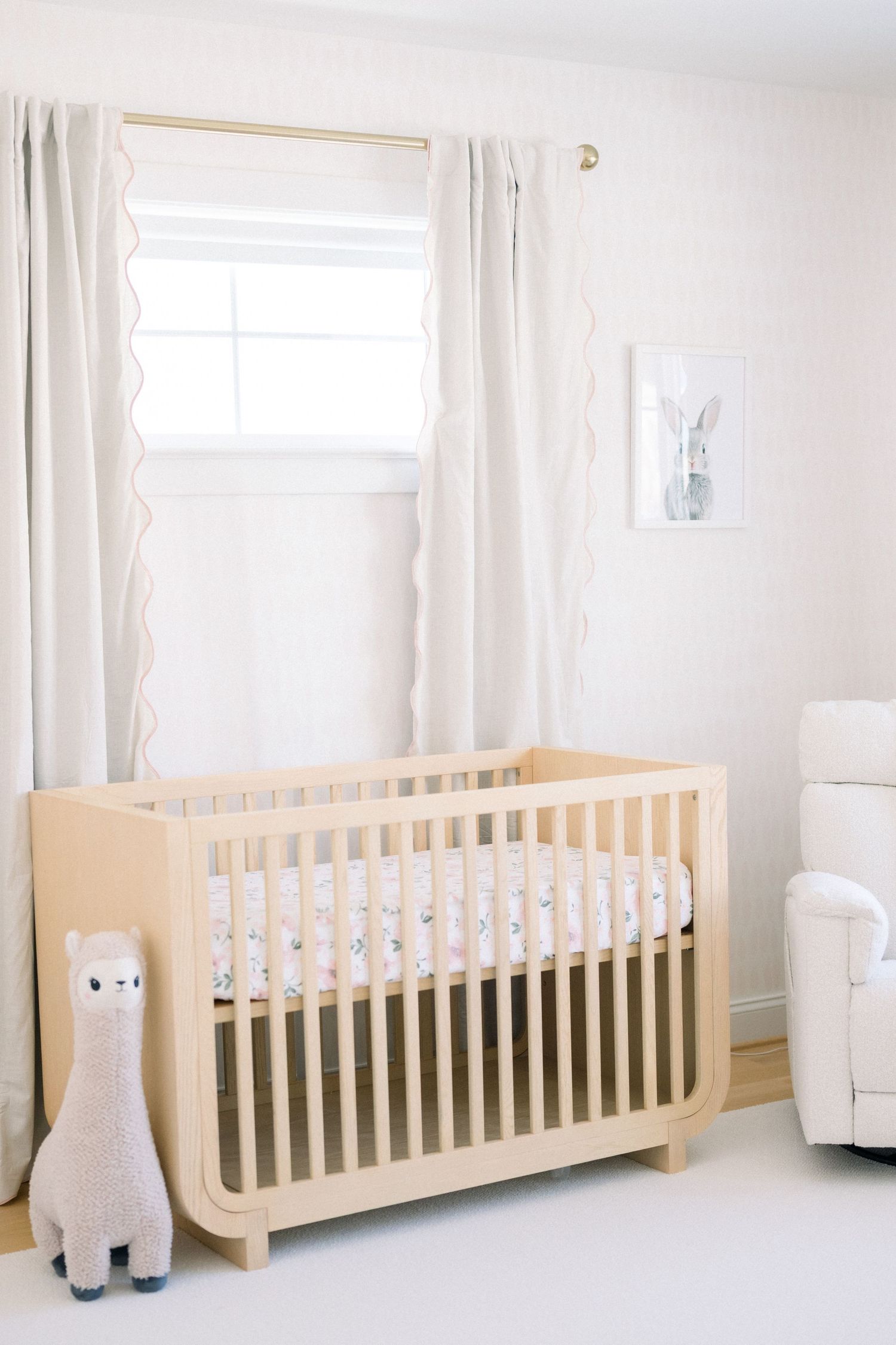 Bright and airy nursery with natural wood cribs, white curtains, and plush animal decor in a minimalist style.