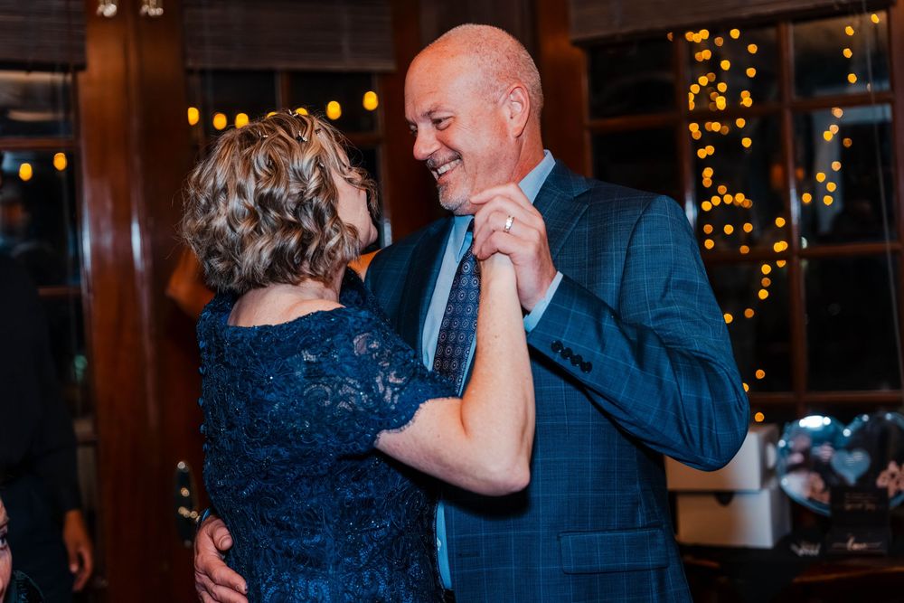 Elegant couple dancing together at a wedding reception with warm bokeh lights in the background.