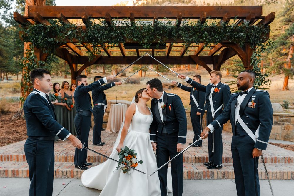 Military wedding couple walking under arch of sabers held by uniformed groomsmen outdoors.