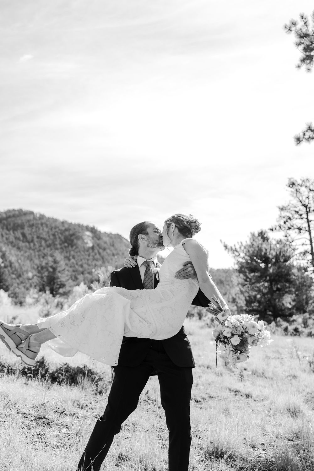 Groom lifts bride for a romantic kiss in a mountain meadow in this black and white wedding portrait.