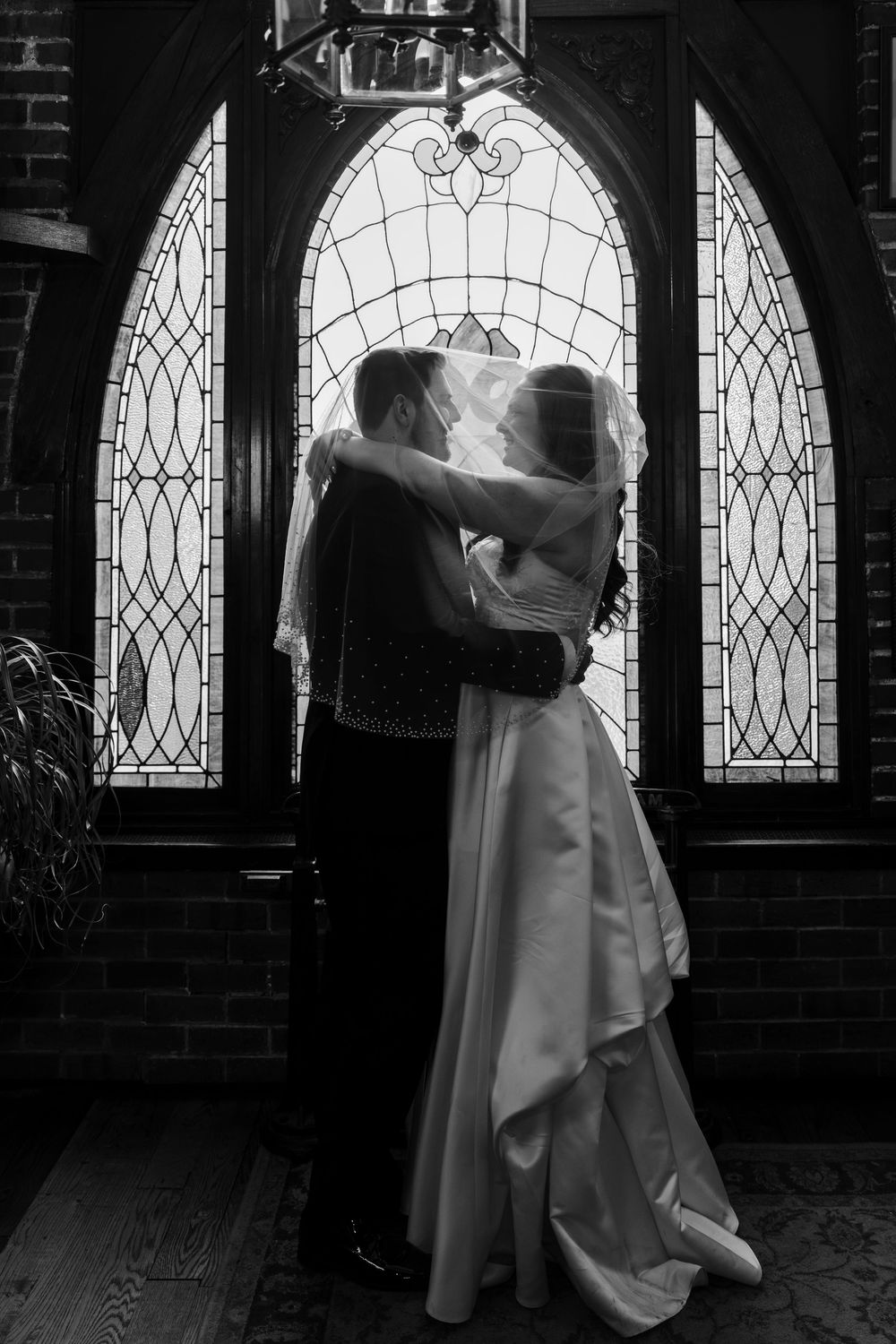 Bride and groom share romantic kiss in front of stained glass church doors.