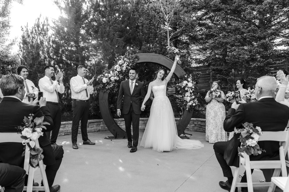 Black and white photo of a joyful bride and groom walking down the aisle after their outdoor wedding ceremony.