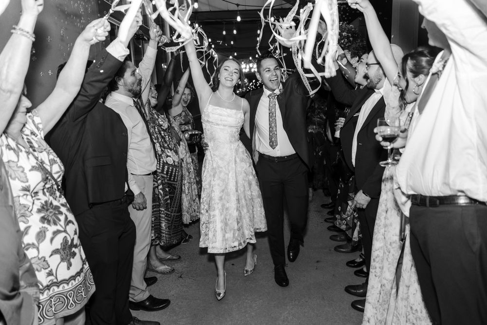 Black and white photo of a bride and groom walking through a celebratory tunnel of guests at their wedding reception.