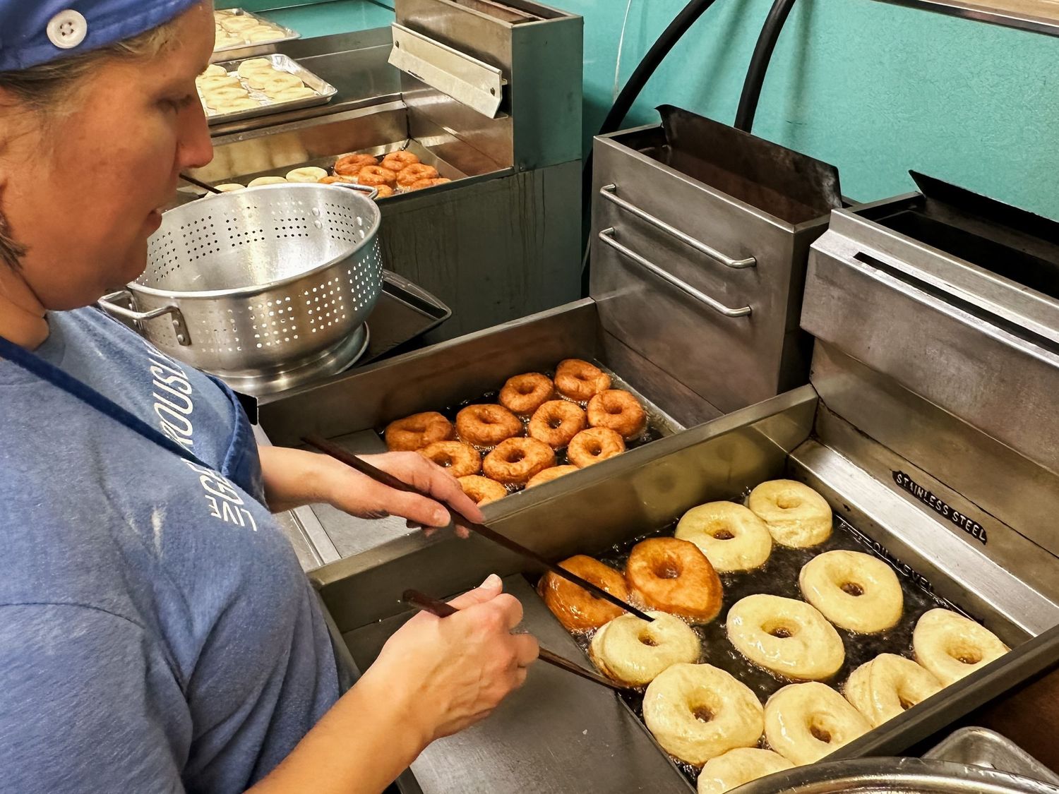A volunteer frying donuts in the kitchen at The Paloma School using chopsticks to flip the homemade donuts.