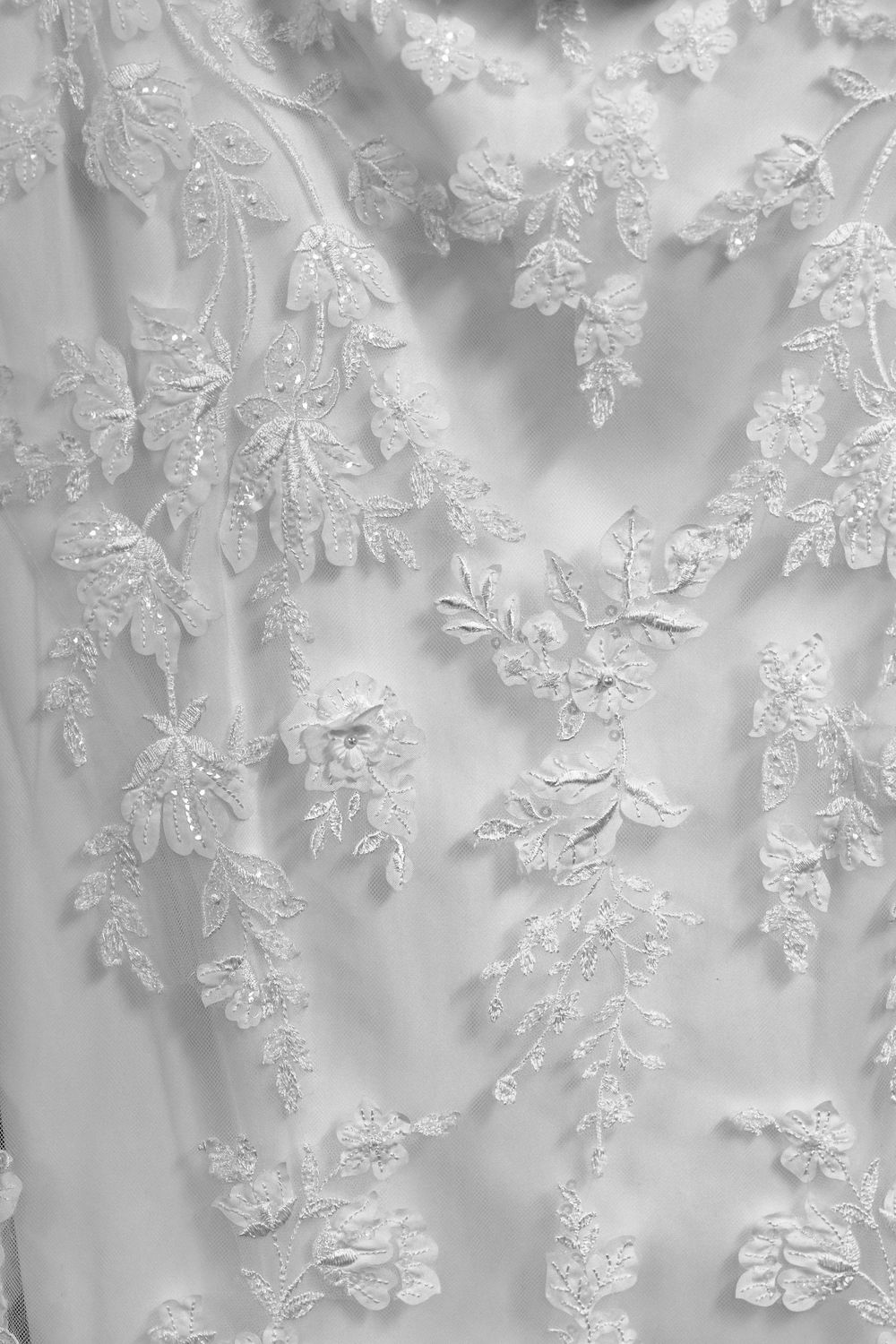 Close-up detail of delicate white lace pattern on wedding dress fabric with floral and leaf designs.