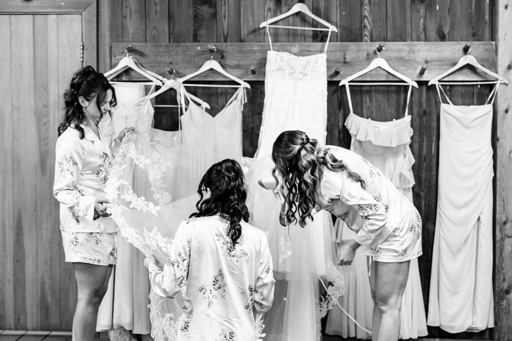 White dresses and robes hanging on wooden hangers against a rustic barn wall background.