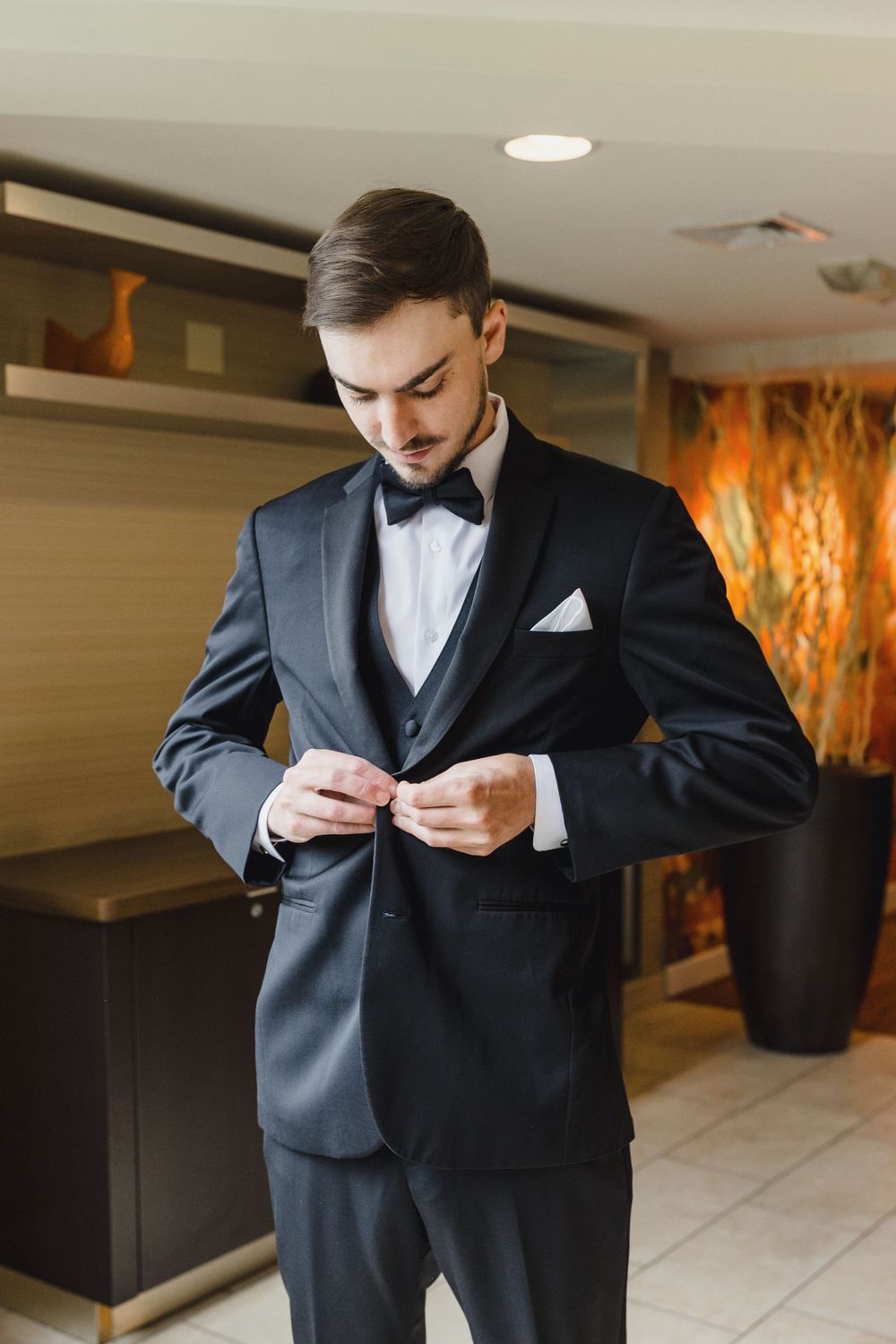 Groom in classic black tuxedo adjusts his bowtie while getting ready.