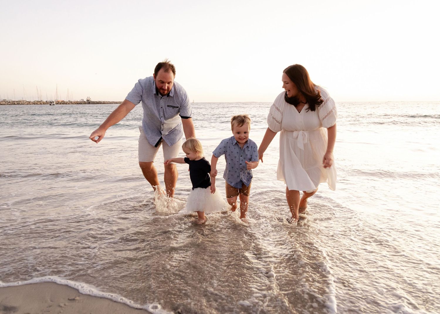A family splashes and plays together in the shallow ocean waves at sunset on a beach.