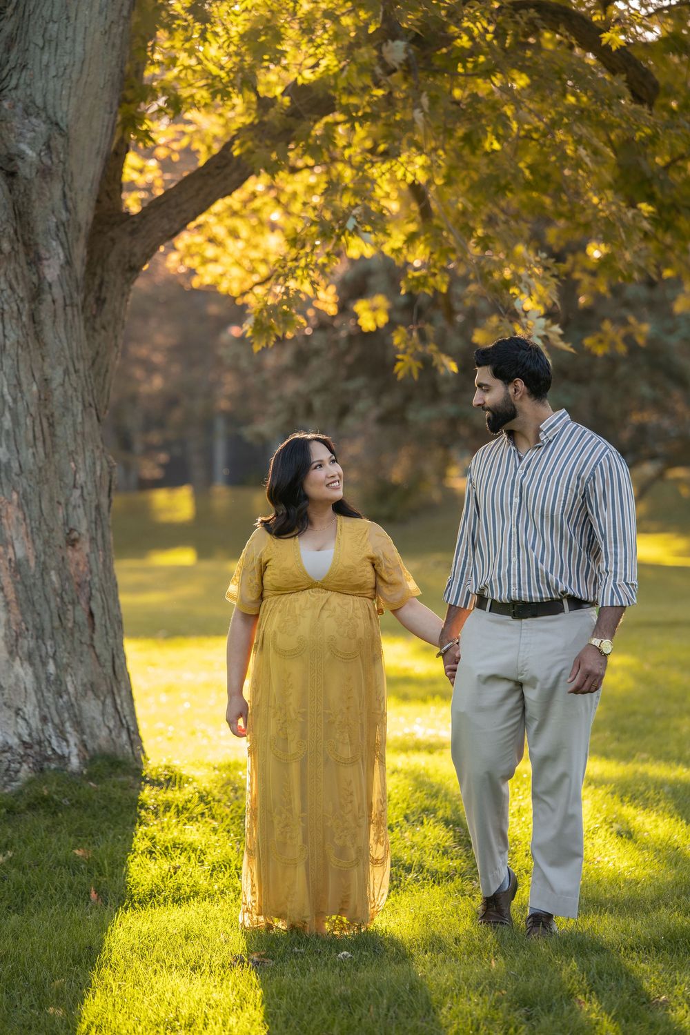 A couple walks together under a golden autumn tree in a sunlit park during sunset.