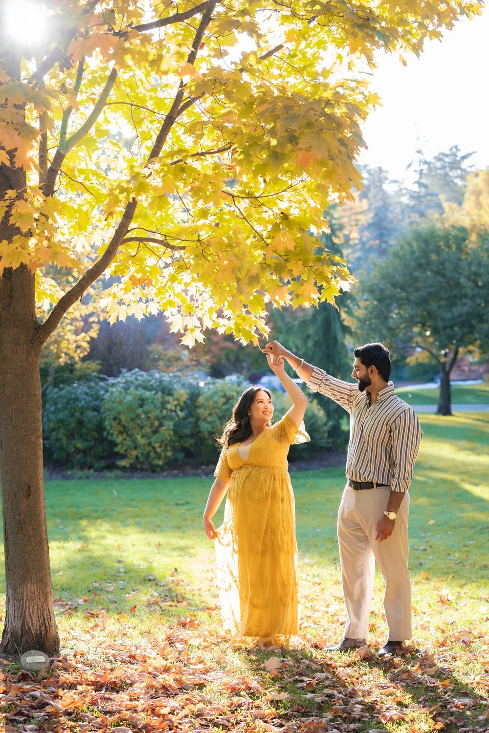 A couple stands under golden autumn trees in a park during sunset, creating a romantic fall atmosphere.