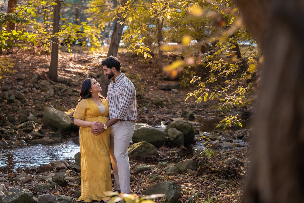 A couple shares a romantic moment together in a wooded autumn setting with golden leaves and natural light.