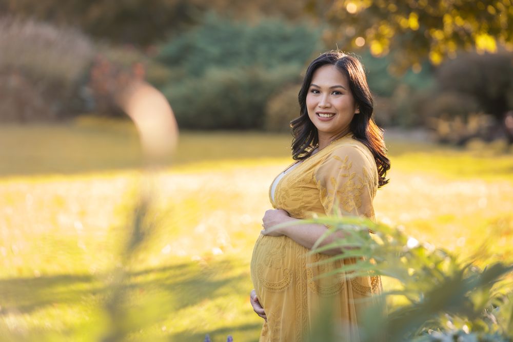A woman in a yellow dress twirls joyfully in a sunlit garden with golden bokeh and ferns in the foreground.