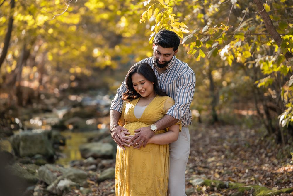 A couple embraces outdoors in autumn with golden leaves and sunlight filtering through the trees.