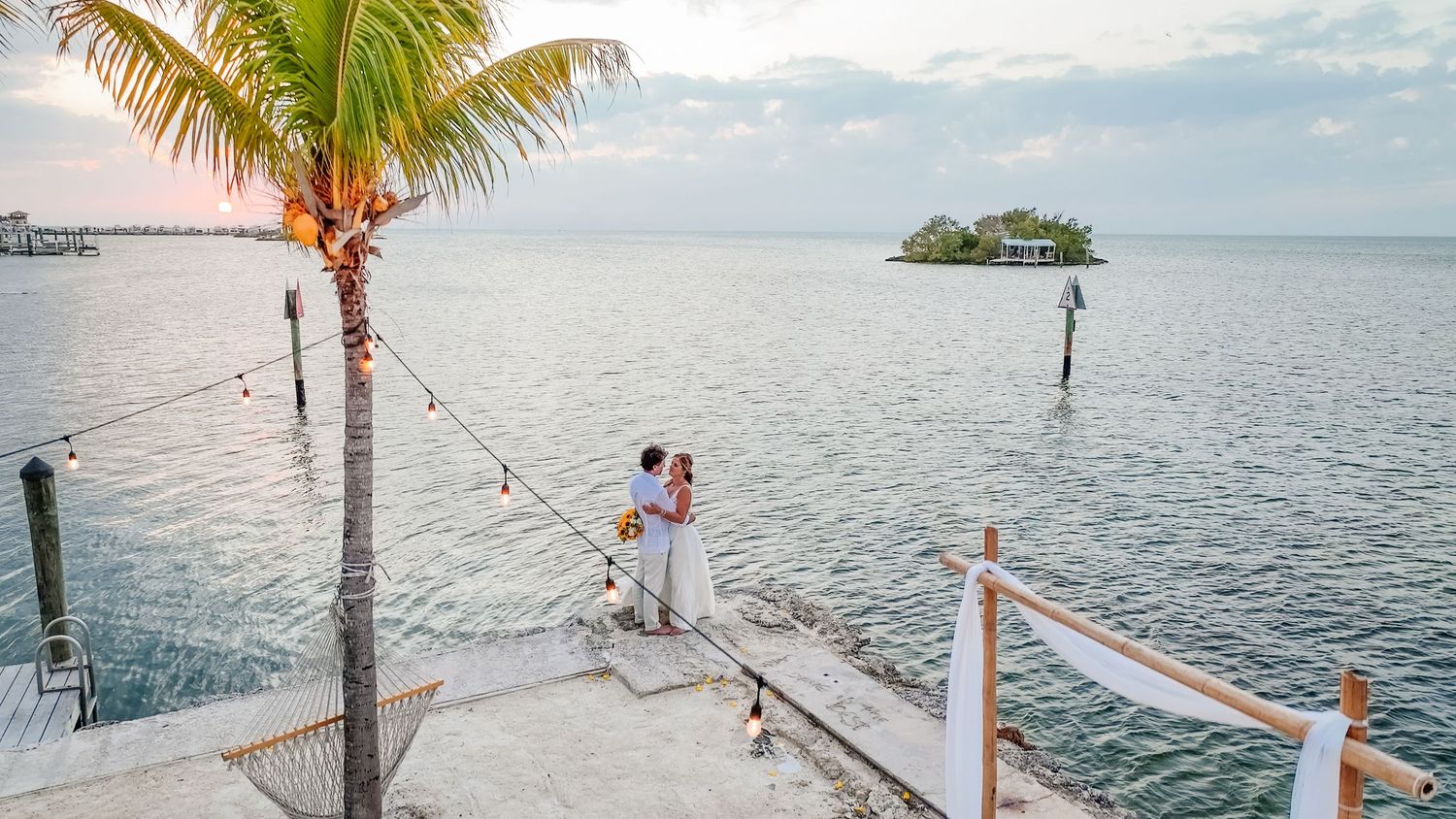 Palm trees line a wooden pier extending over turquoise waters at a tropical beach resort destination.