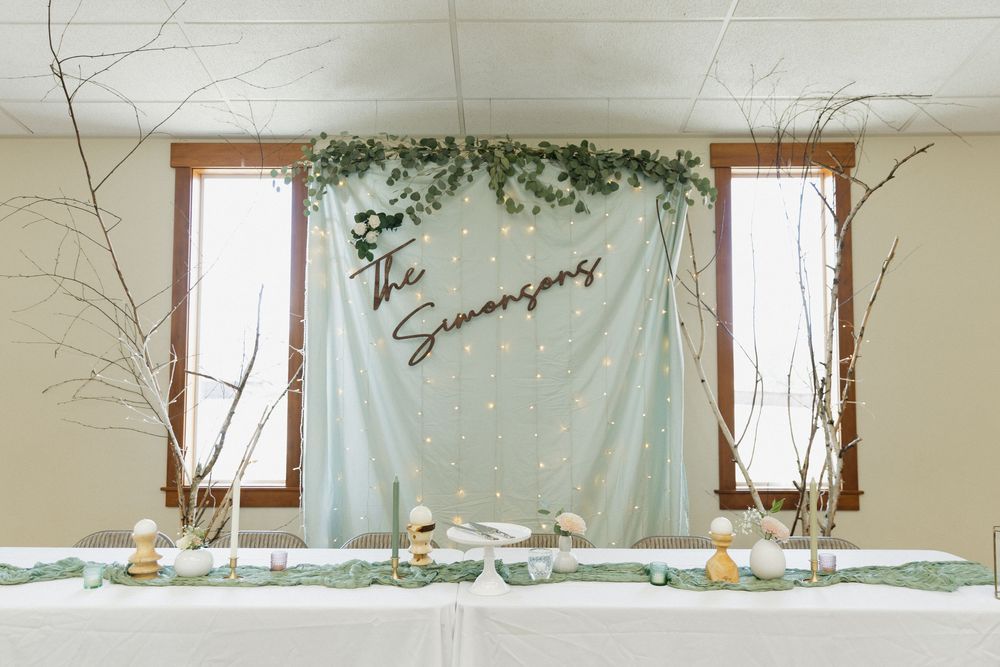 Elegant wedding reception table setup with sage green backdrop, twinkle lights, and natural branch decorations.
