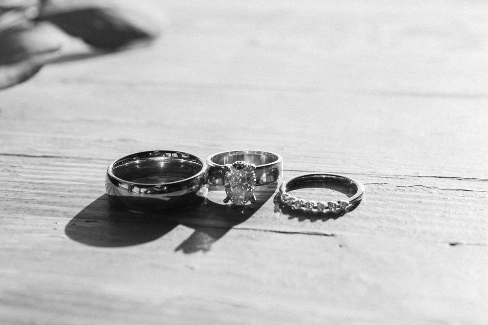 Three wedding rings casting shadows on a light wooden surface in black and white.