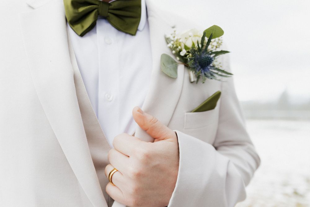 A green bowtie and floral boutonniere accent a crisp white suit jacket.