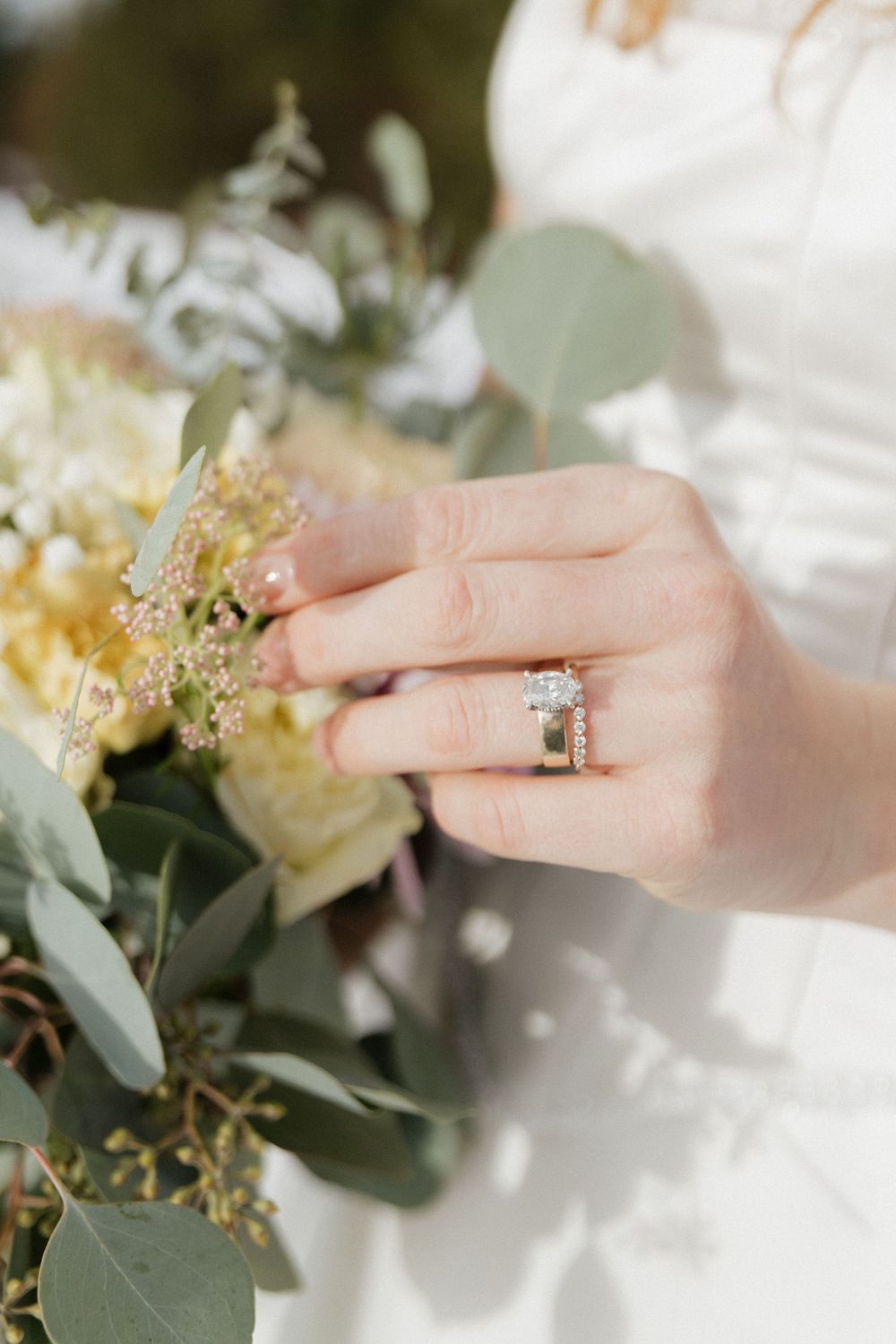 Close-up detail of an engagement ring with delicate floral arrangements and eucalyptus leaves in soft lighting.