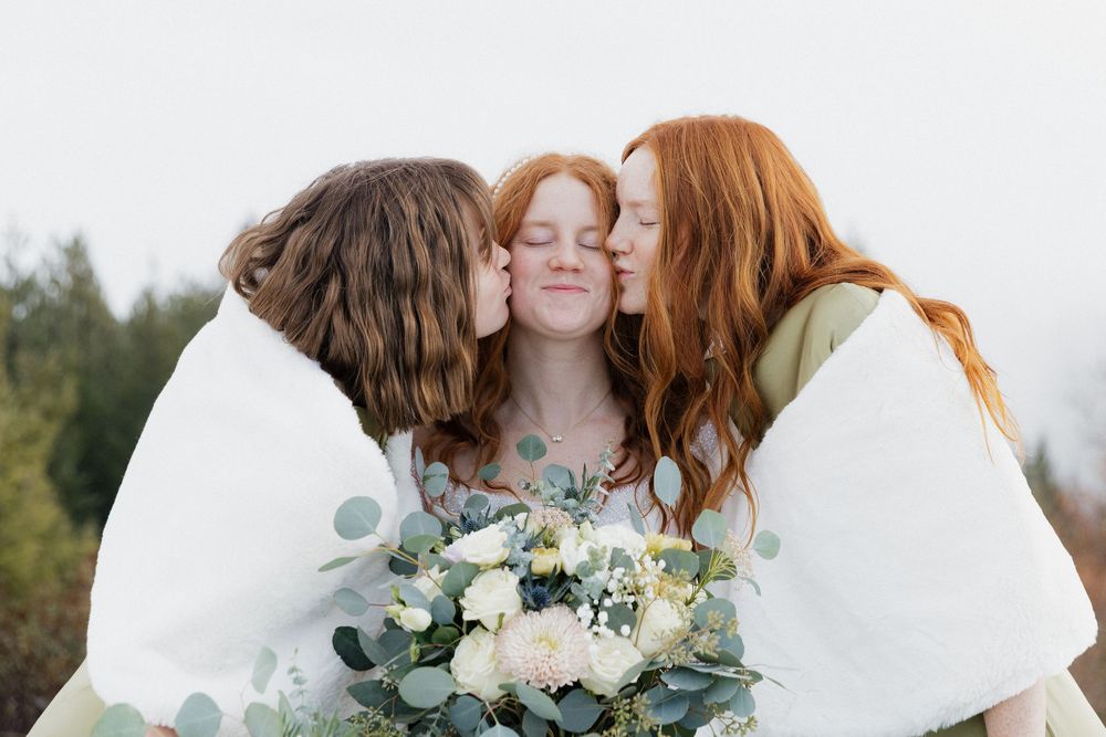Three people sharing a tender moment with white flowers and eucalyptus bouquet outdoors.