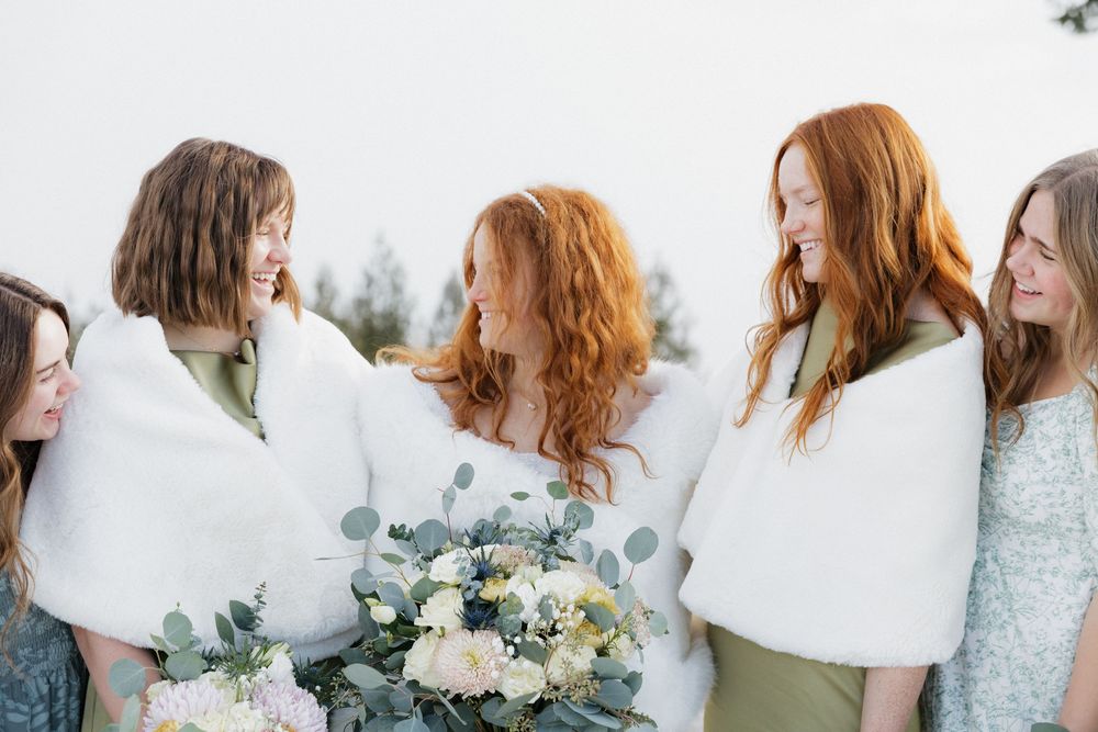 A group of bridesmaids in white and light blue dresses pose together outdoors at a wedding celebration.