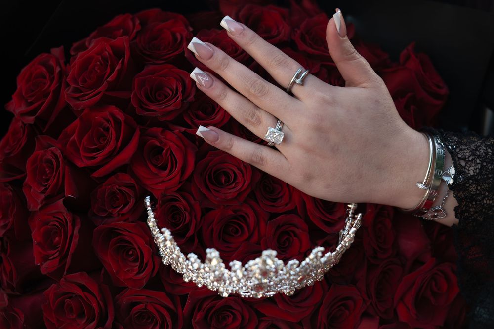 A silver rhinestone tiara displayed against a backdrop of deep red roses.