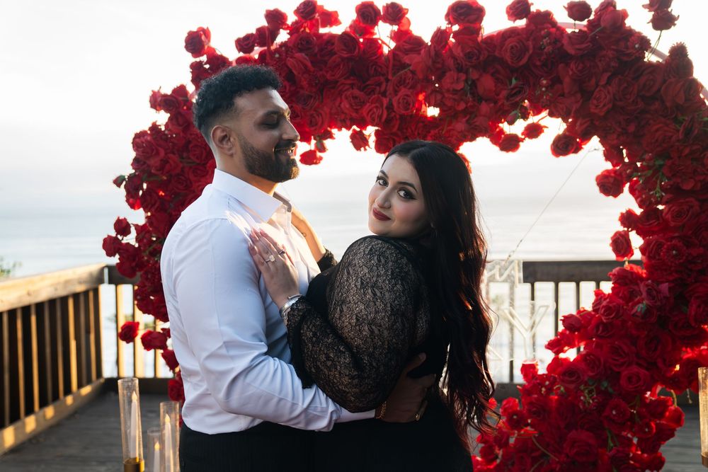 A romantic couple embraces under vibrant red floral arches during a sunset photoshoot.