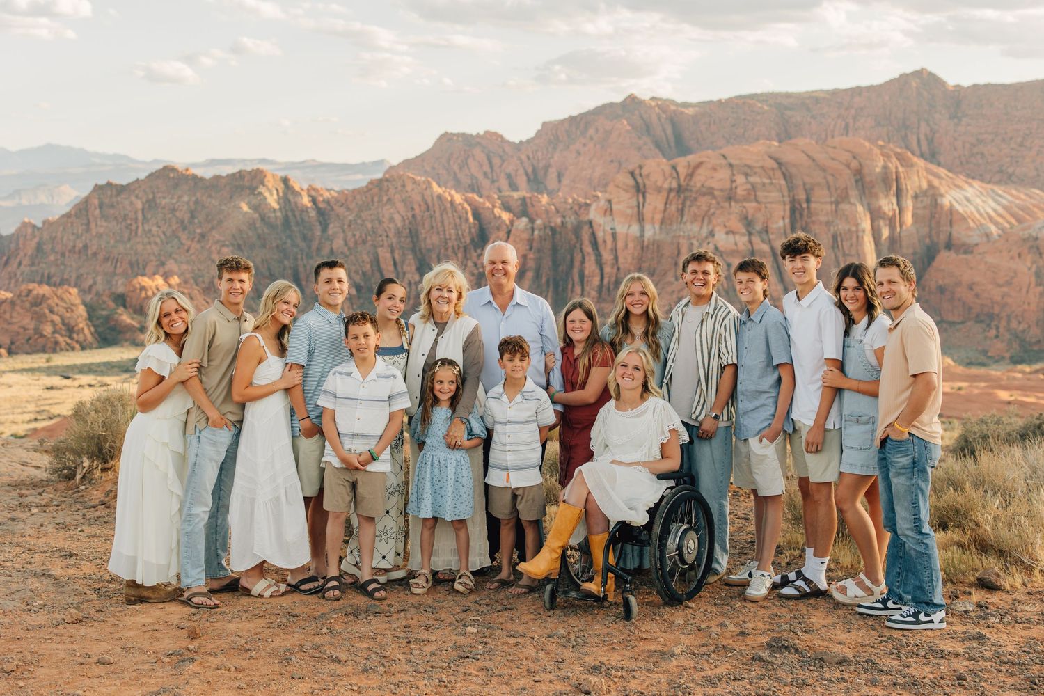 A group of people stand together against a backdrop of dramatic red rock cliffs in a desert landscape during sunset.