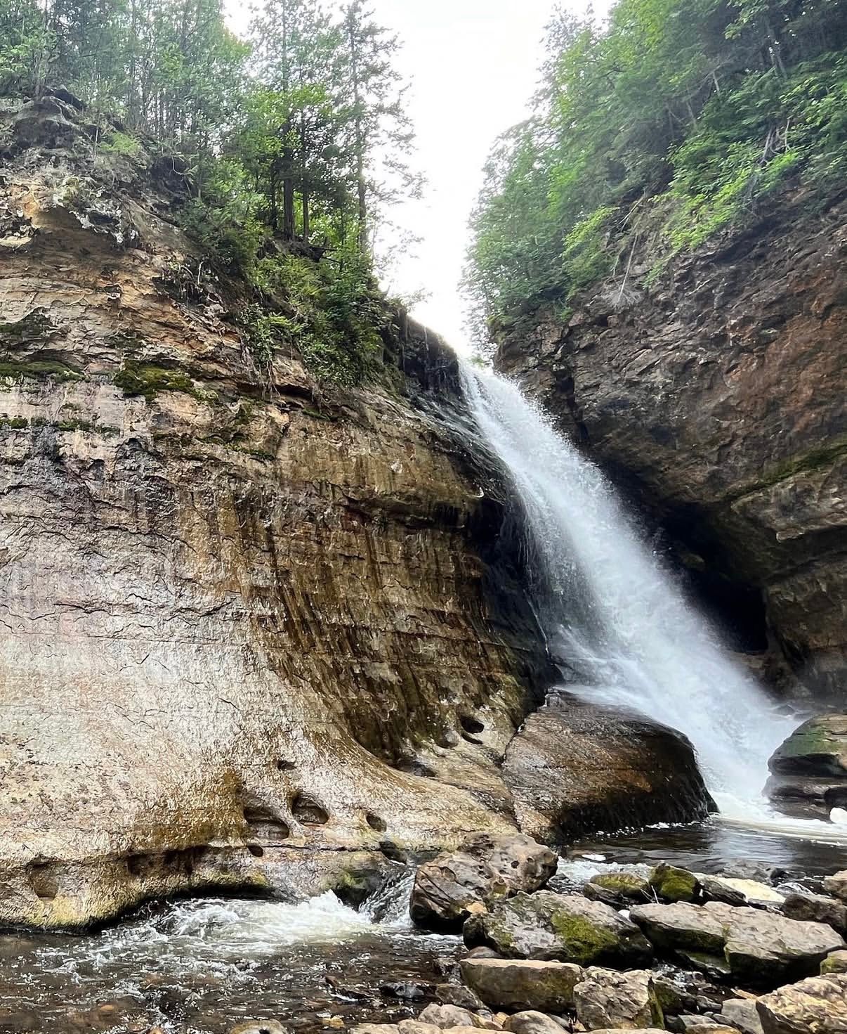 Dramatic waterfall cascading down sandstone cliffs in a lush forest setting.