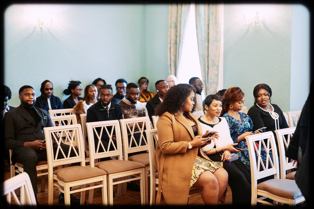 A row of white wooden chairs arranged in a church or event space with people seated during a ceremony.