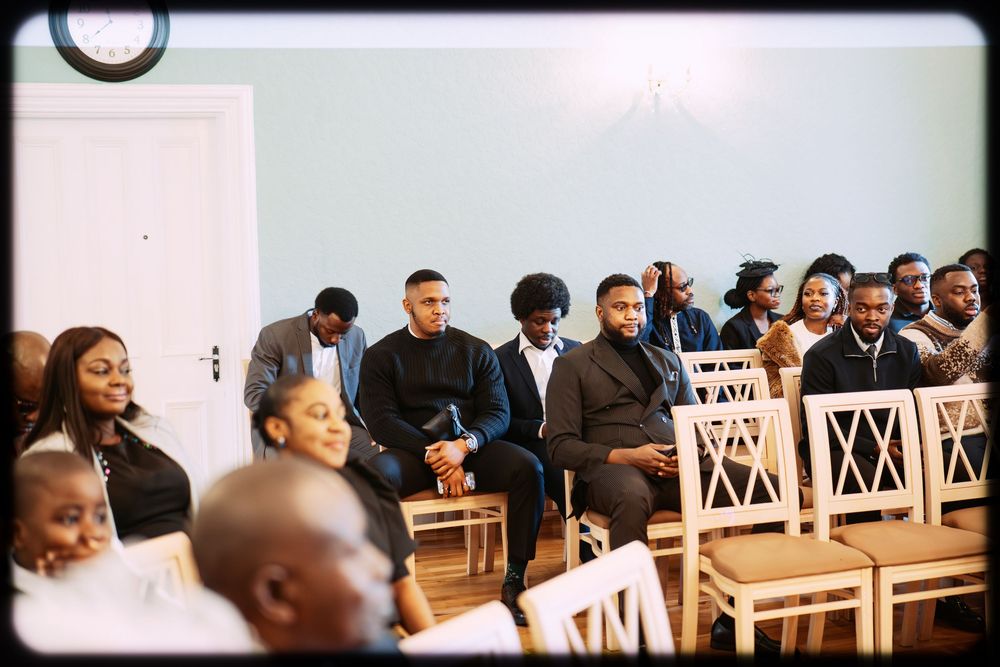 A row of people seated in wooden chairs at a meeting or conference in a bright room.