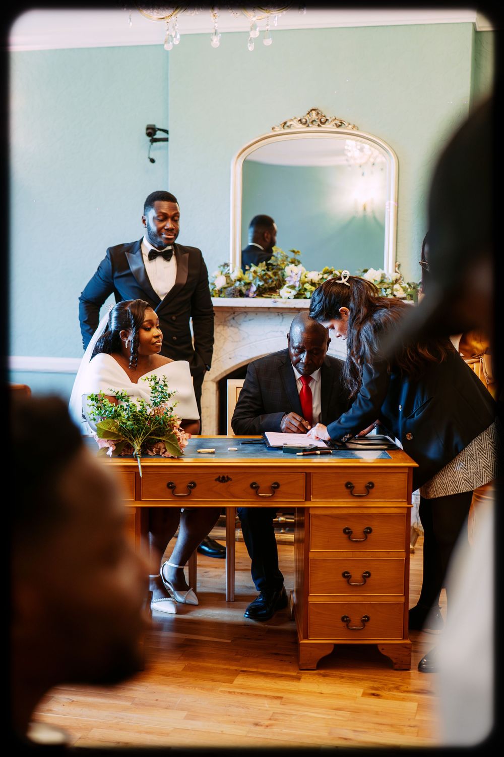 Wedding party members gather around a wooden dresser during a formal celebration in an elegant room.