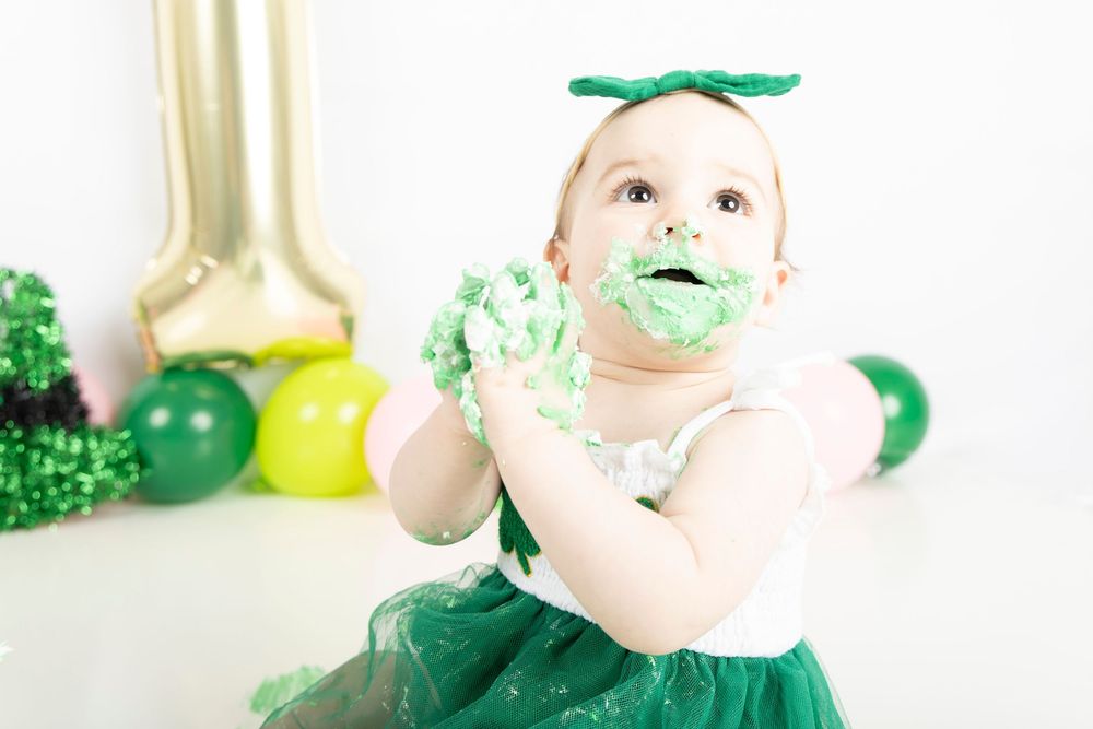 A series of photos showing messy green frosting smeared on a highchair tray and baby during cake smashing session.