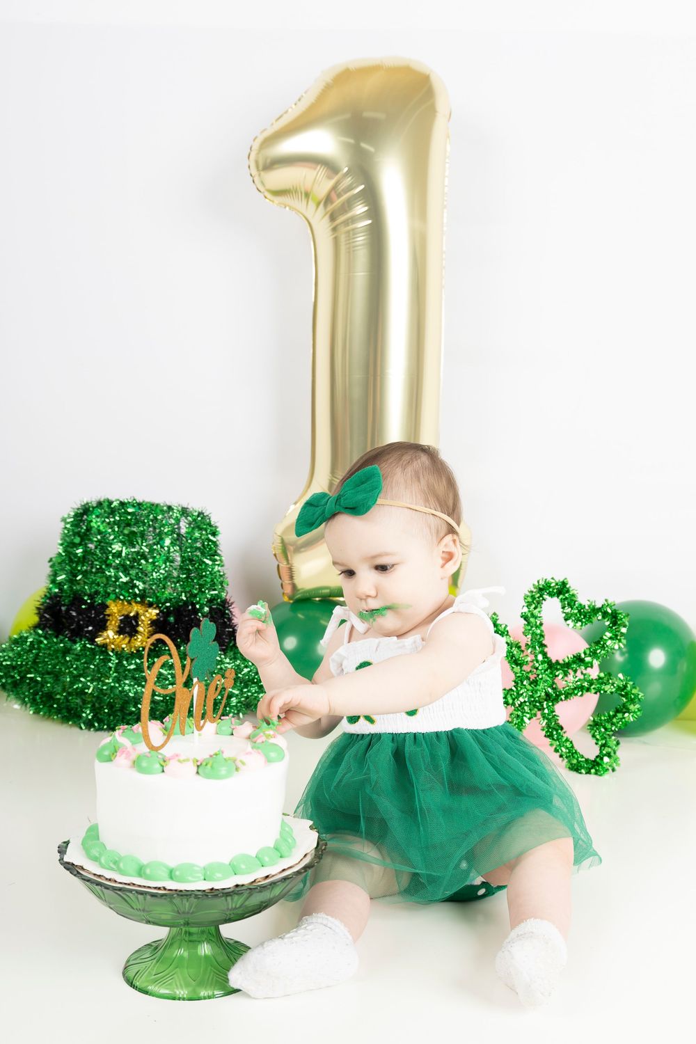 A first birthday celebration with green decorations, gold balloon, and white cake with shamrock details.