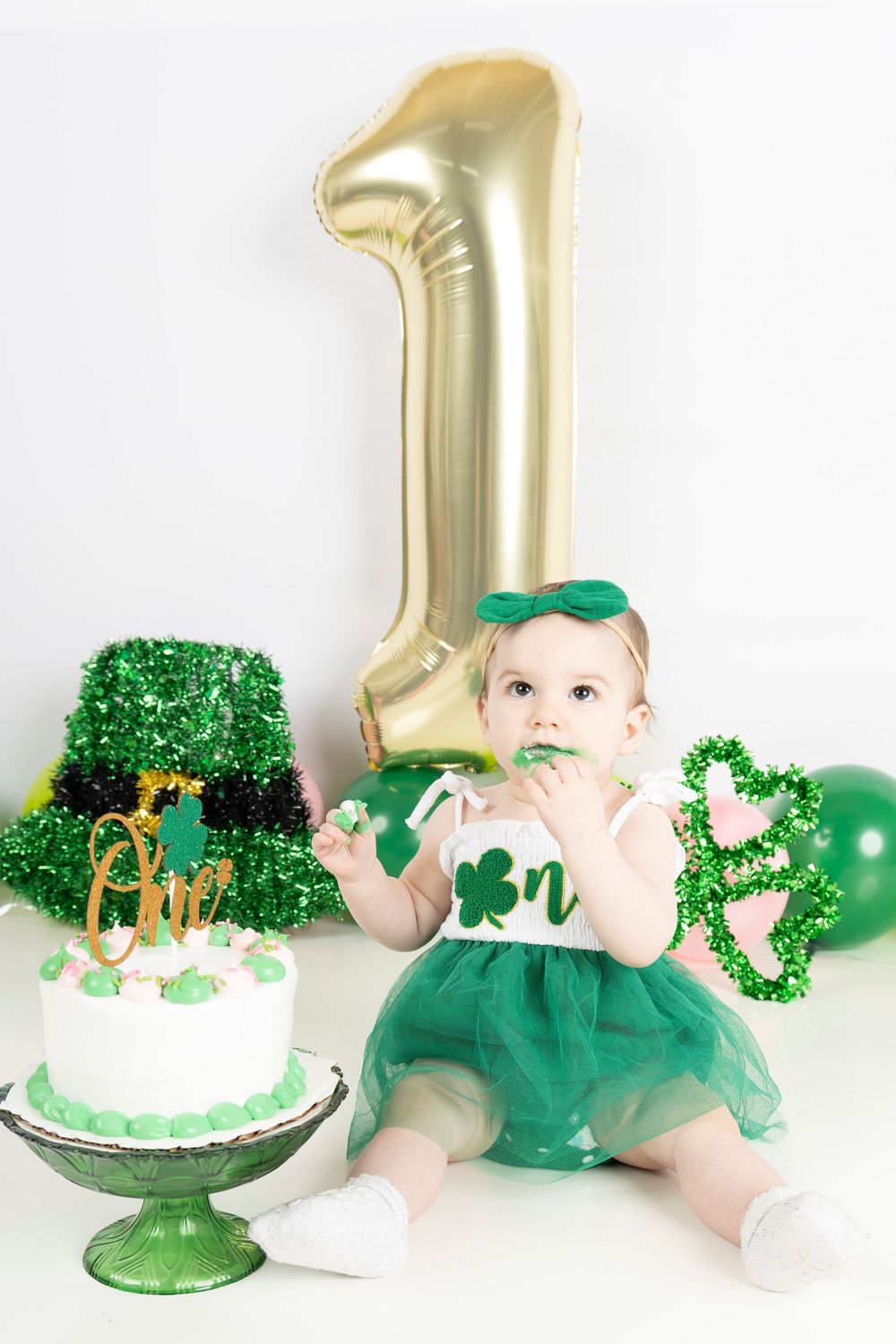 St Patrick's Day first birthday celebration setup with gold balloon number one, green cake and party decorations.