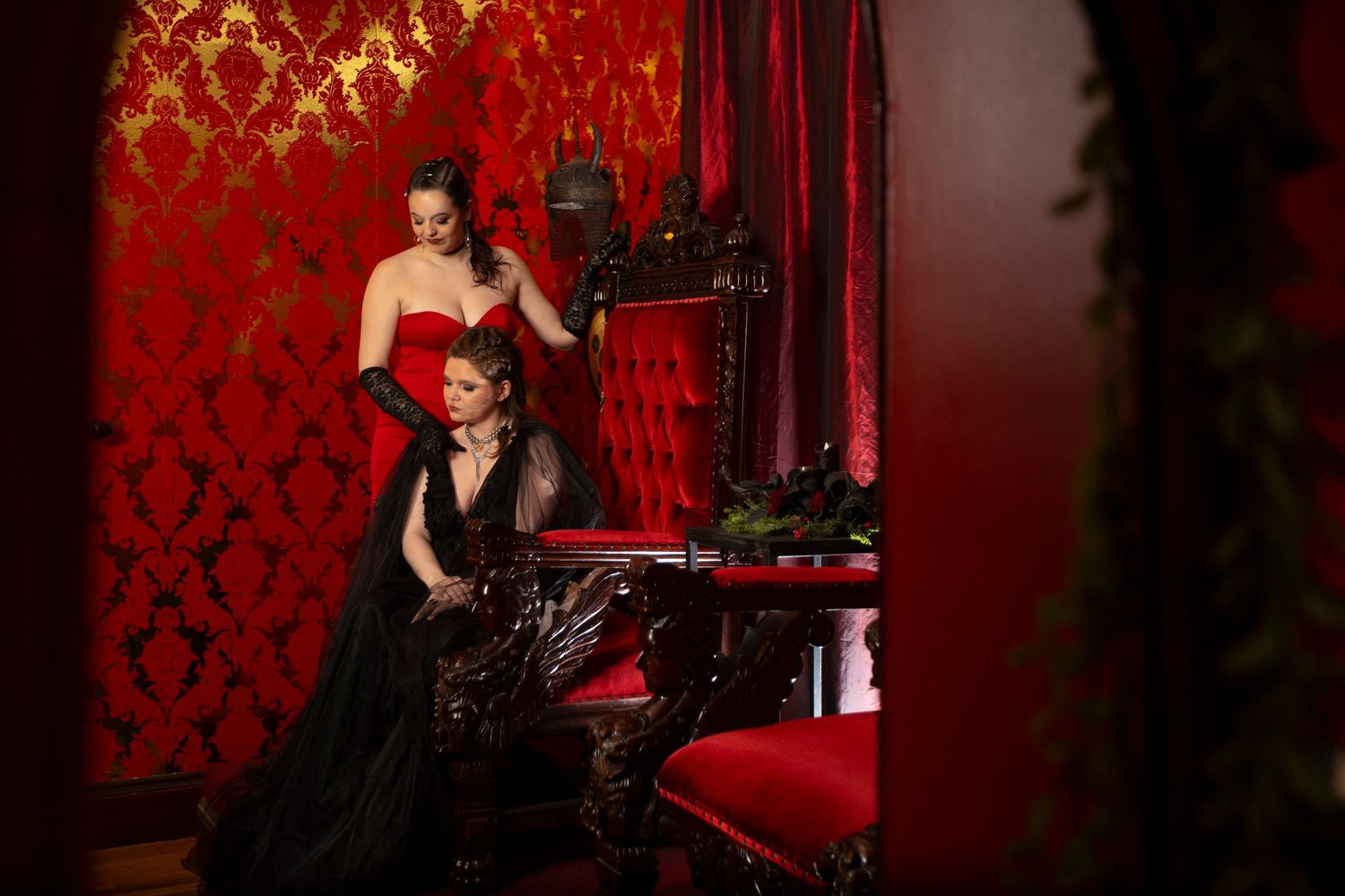 Glamorous photo shoot in a luxurious red room with vintage furniture and dramatic lighting.