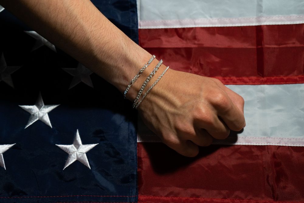 A hand holds a voting ballot against an American flag background in red white and blue colors.