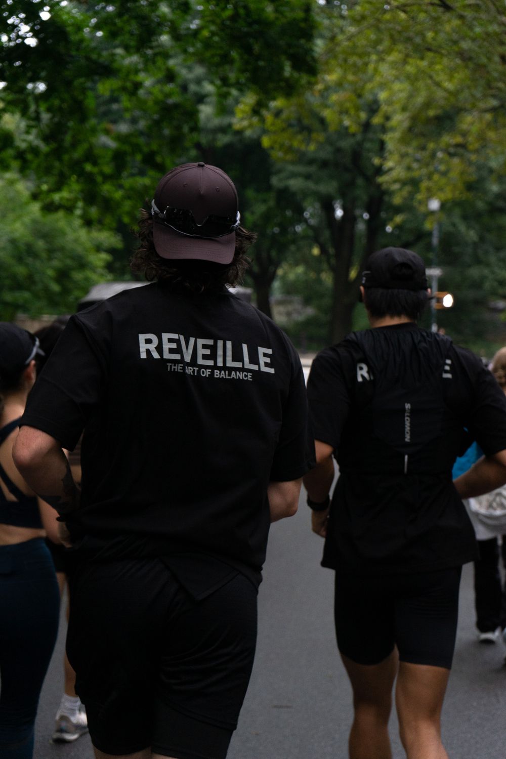 A group of people wearing black shirts walking on a path with one shirt displaying 'REVEILLE' text on the back.