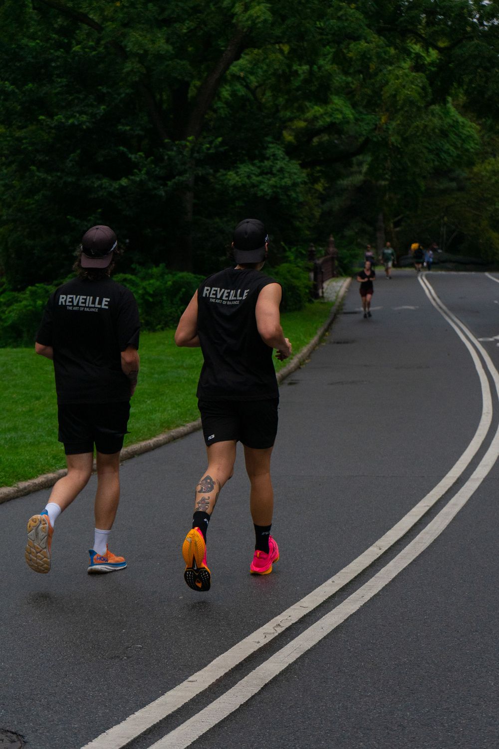 People in black workout clothes walking on a curved asphalt path through a green park setting.