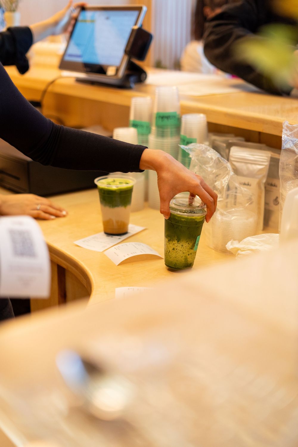 People sitting at a wooden table with drinks and small green containers in a casual dining setting.