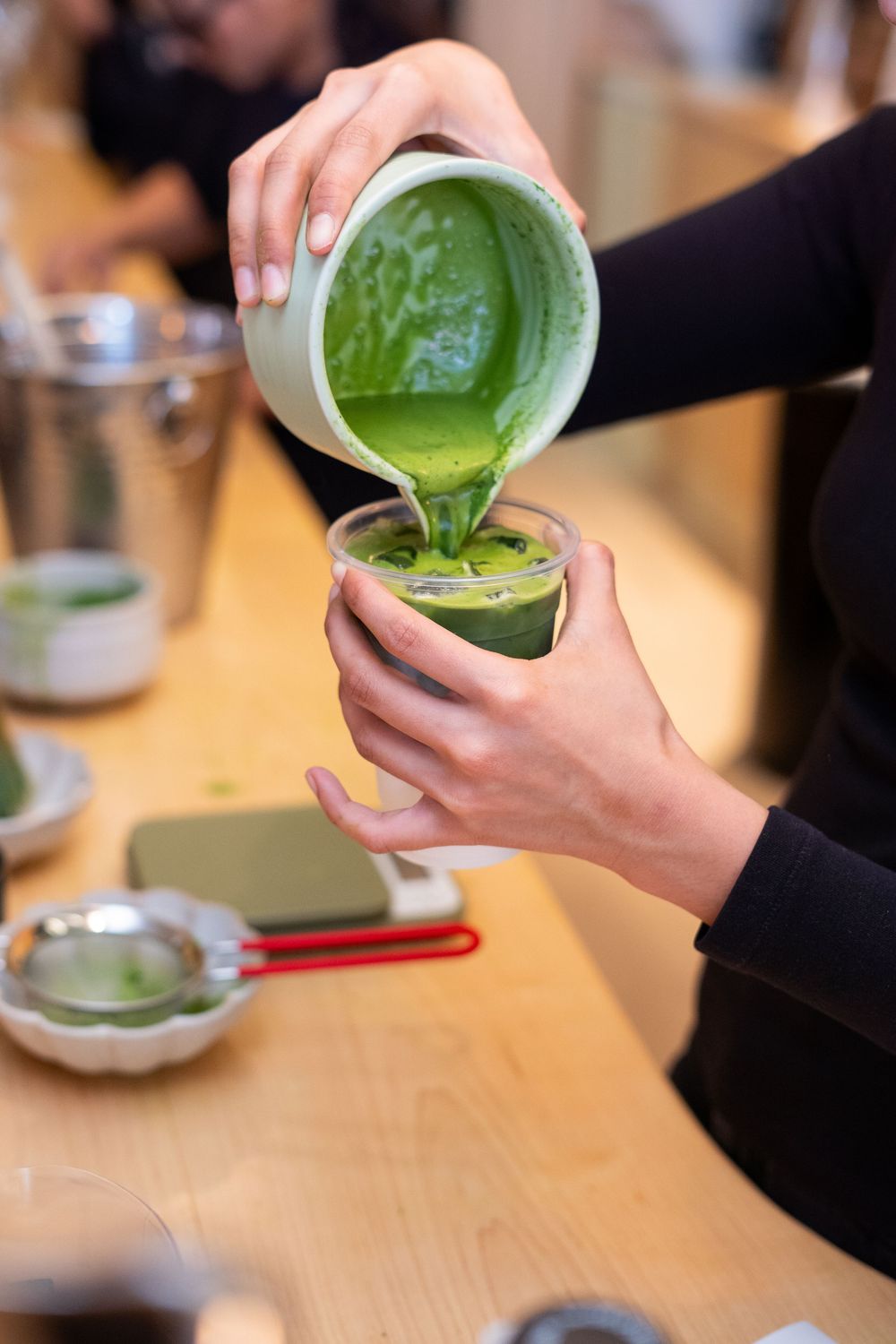 Hands pouring bright green matcha tea from traditional bowls in a sequence of preparation steps on wooden table.