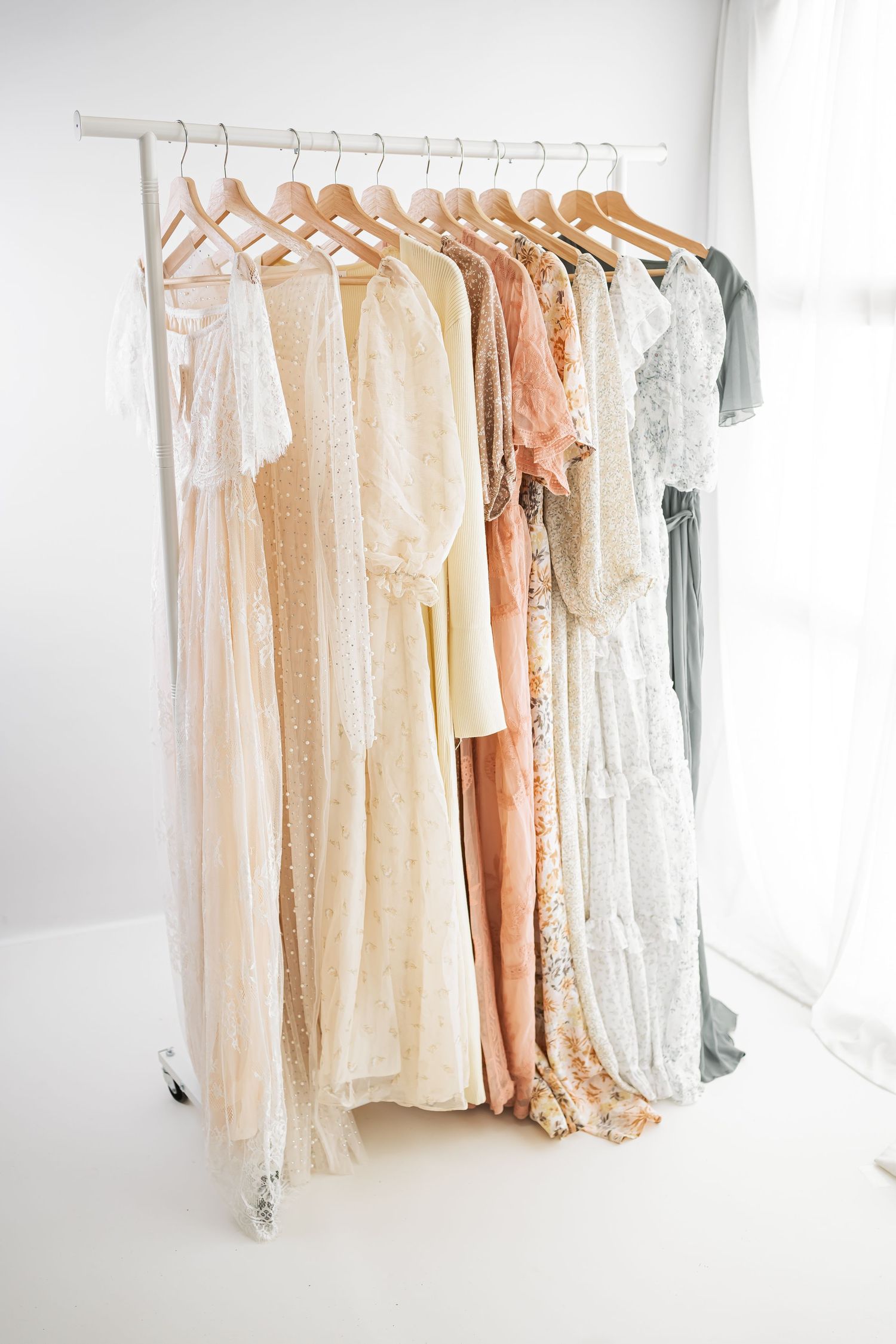 A collection of pastel and neutral colored dresses hanging on white clothing racks in a bright, airy space.