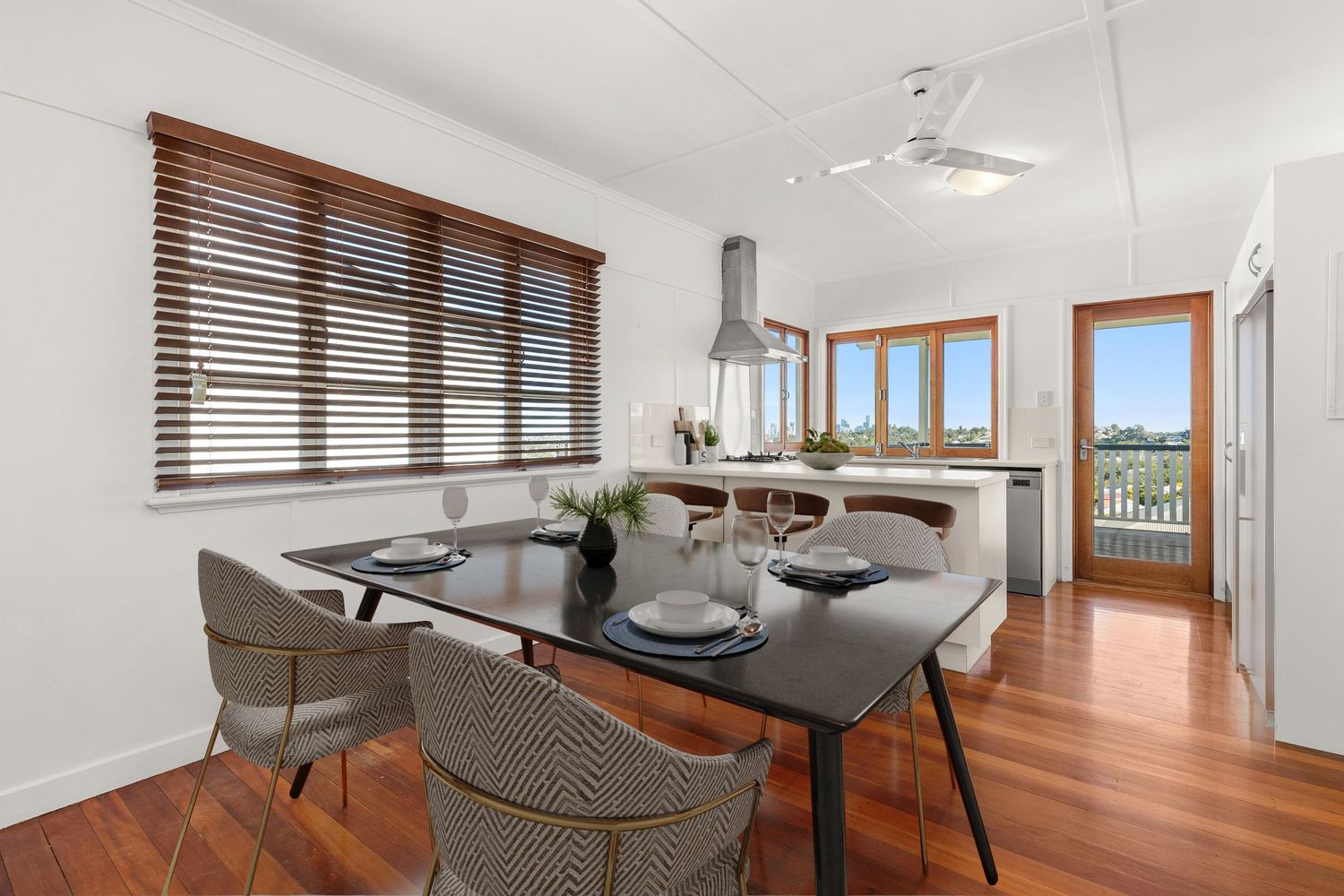 Bright dining room with timber floors, wooden blinds, and black dining table.