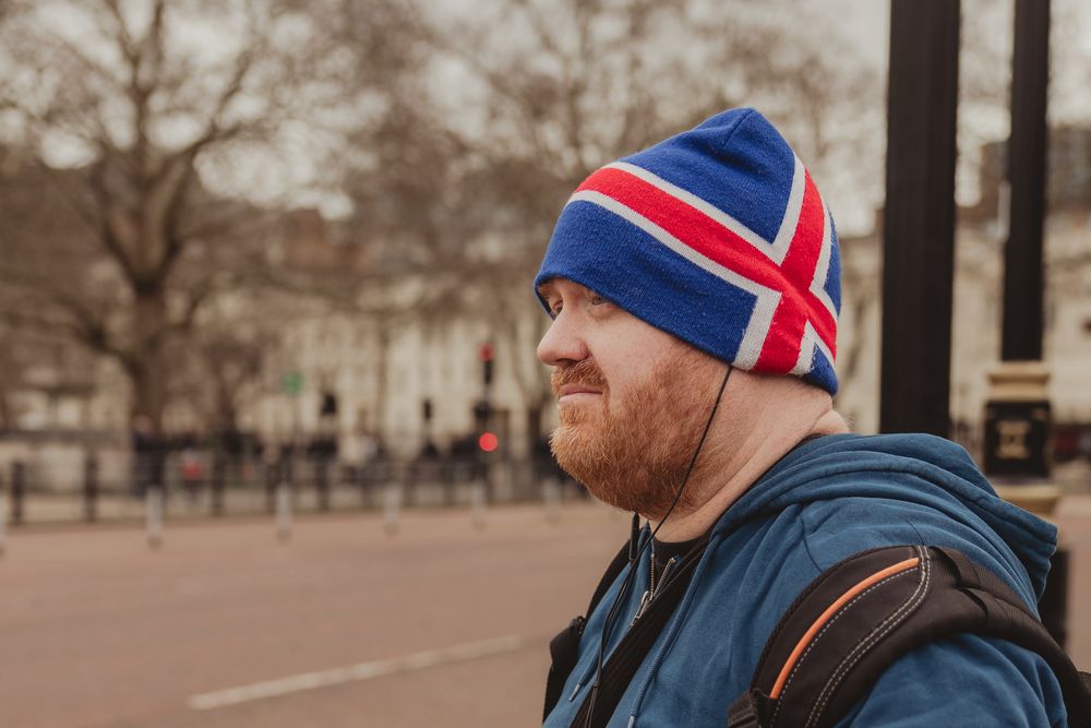 A person wearing a Union Jack beanie hat and navy jacket stands outdoors on a cloudy winter day in London.